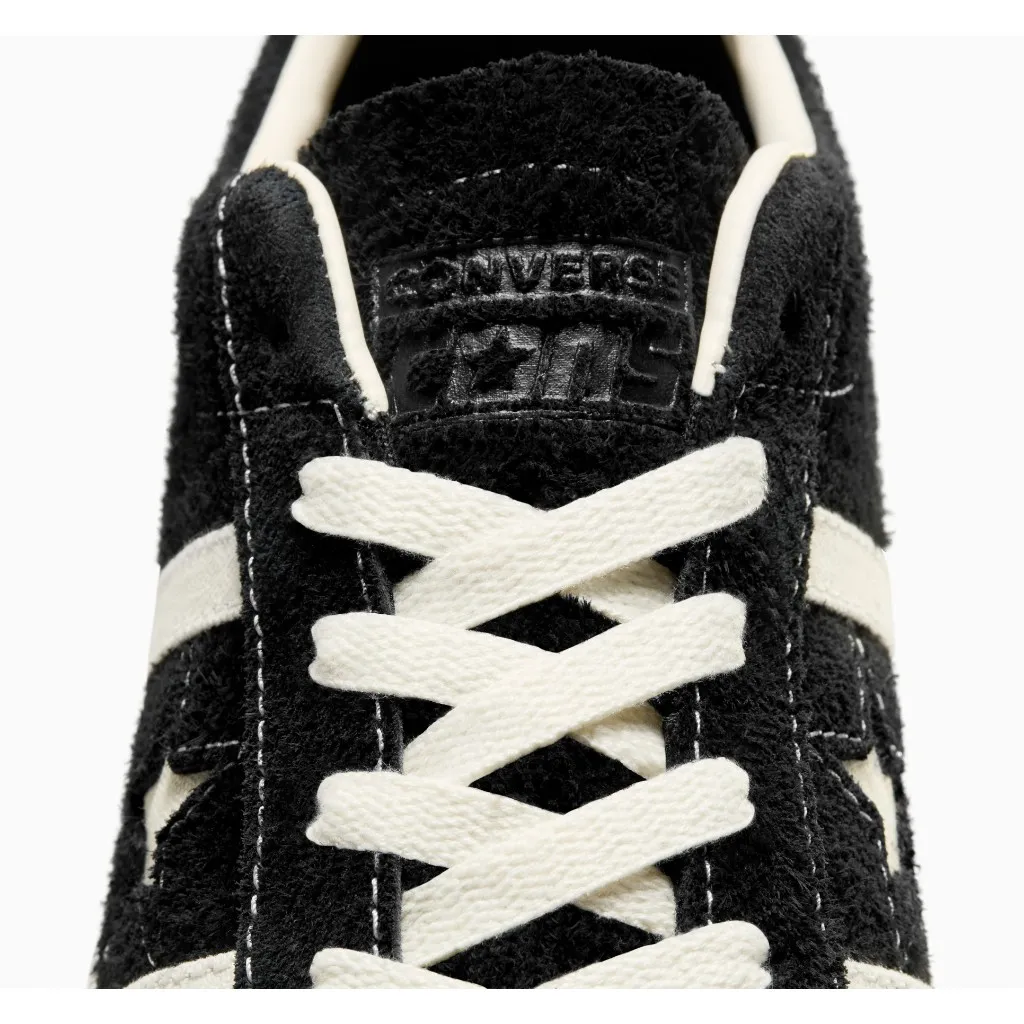 มุมมองระยะใกล้ของส่วนบนของรองเท้าผ้าใบสีดำ แสดงเชือกผูกรองเท้าสีขาว โลโก้ Converse และดาวบนลิ้นรองเท้า