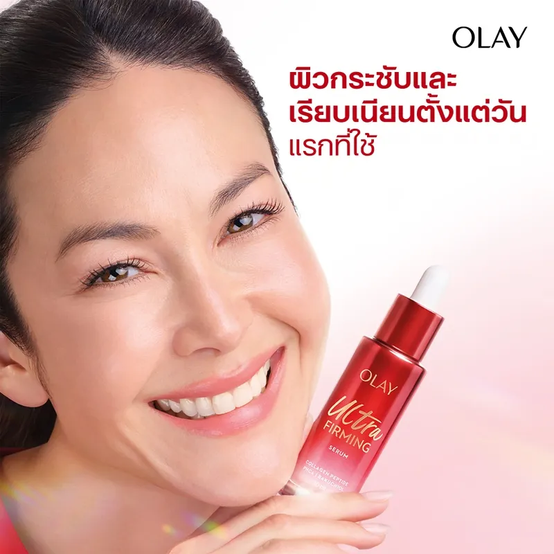 ผู้หญิงยิ้มถือ Olay Ultra Firming Serum ขวดสีแดง โทนพื้นหลังชมพูอ่อน