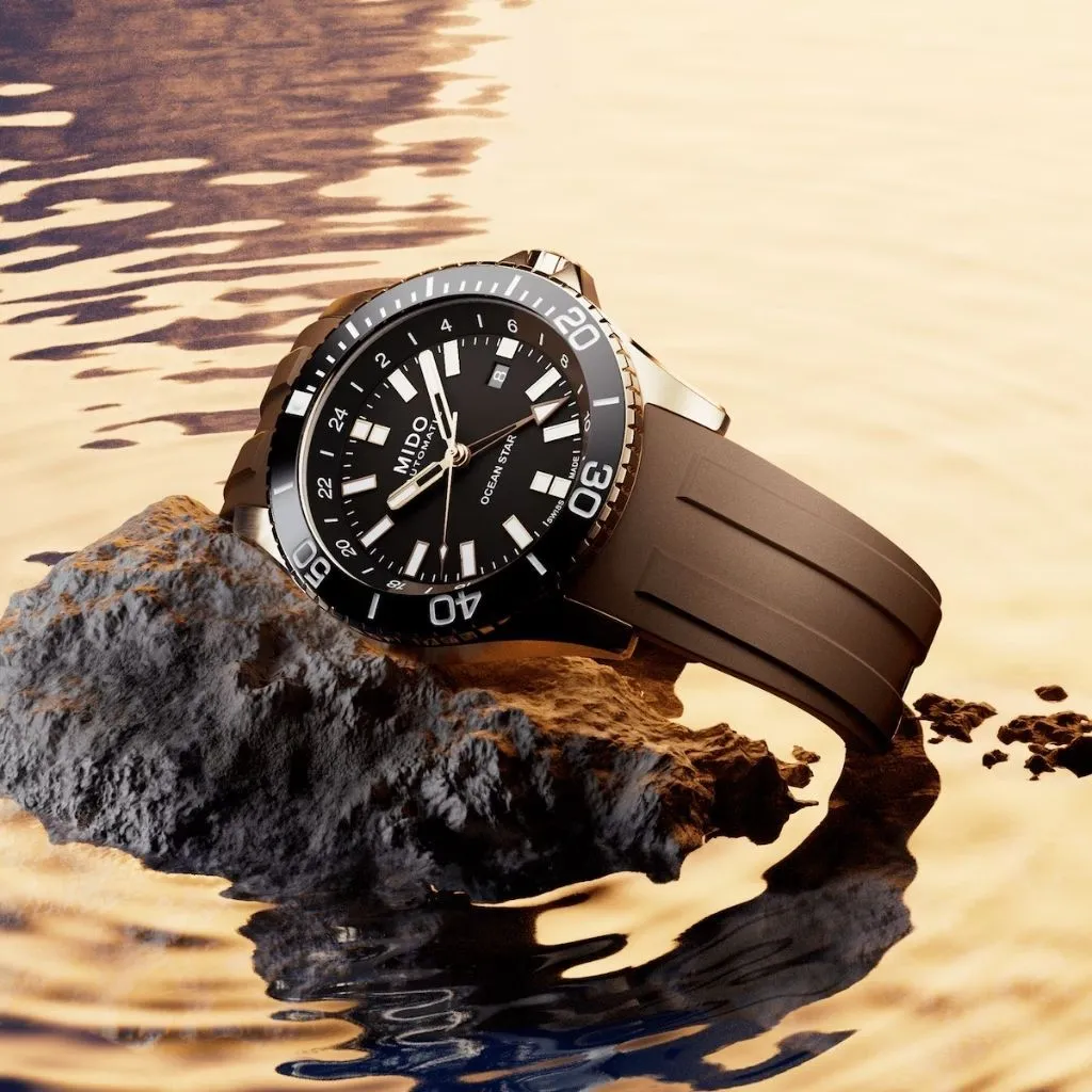 MIDO Ocean Star GMT M0266293729100 วางบนโขดหินริมผิวน้ำ โทนพระอาทิตย์ตก สายยางสีน้ำตาล