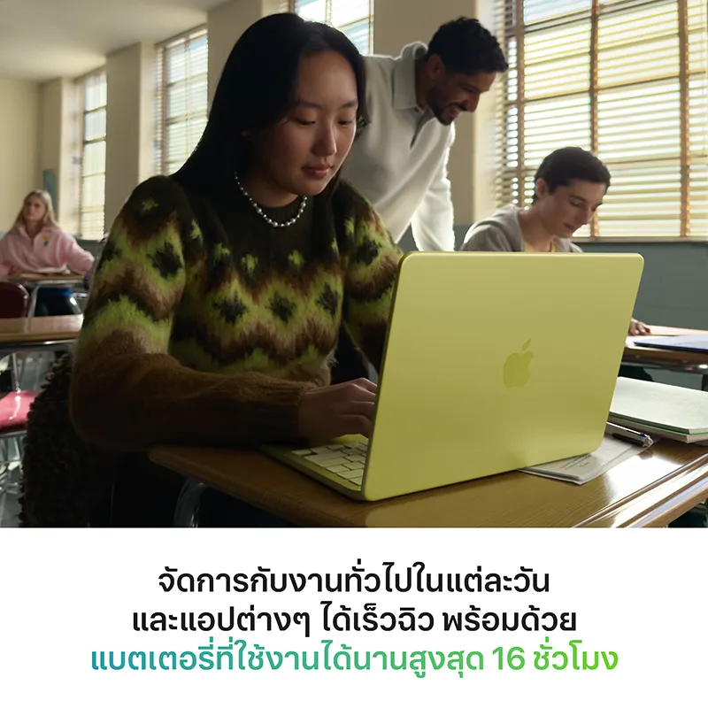 นักเรียนหญิงนั่งพิมพ์งานบนตัวเครื่องสีเหลืองในห้องเรียน ขณะครูยืนดูด้านหลัง และมีข้อความแบตเตอรี่ 16 ชั่วโมง