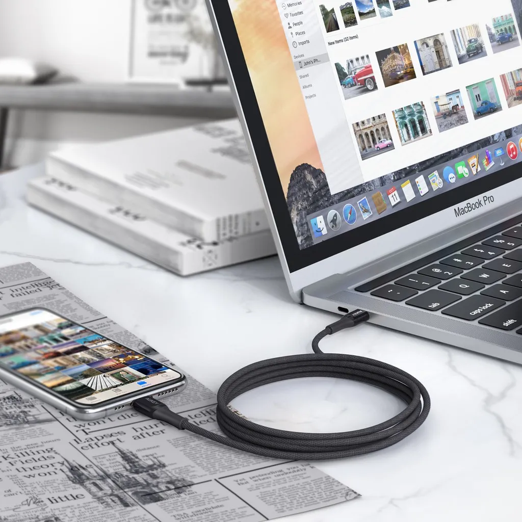 อุปกรณ์เชื่อมต่อสีดำใช้งานกับ iPhone และ MacBook บนโต๊ะทำงานสำหรับถ่ายโอนข้อมูล
